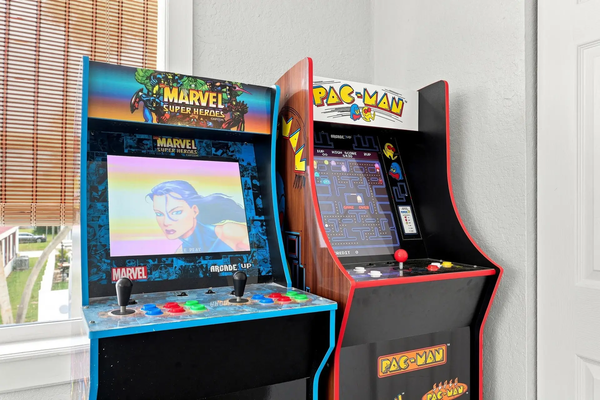 Marvel Super Heroes and Pac-Man stand-up arcade cabinets side by side beside a shuttered window