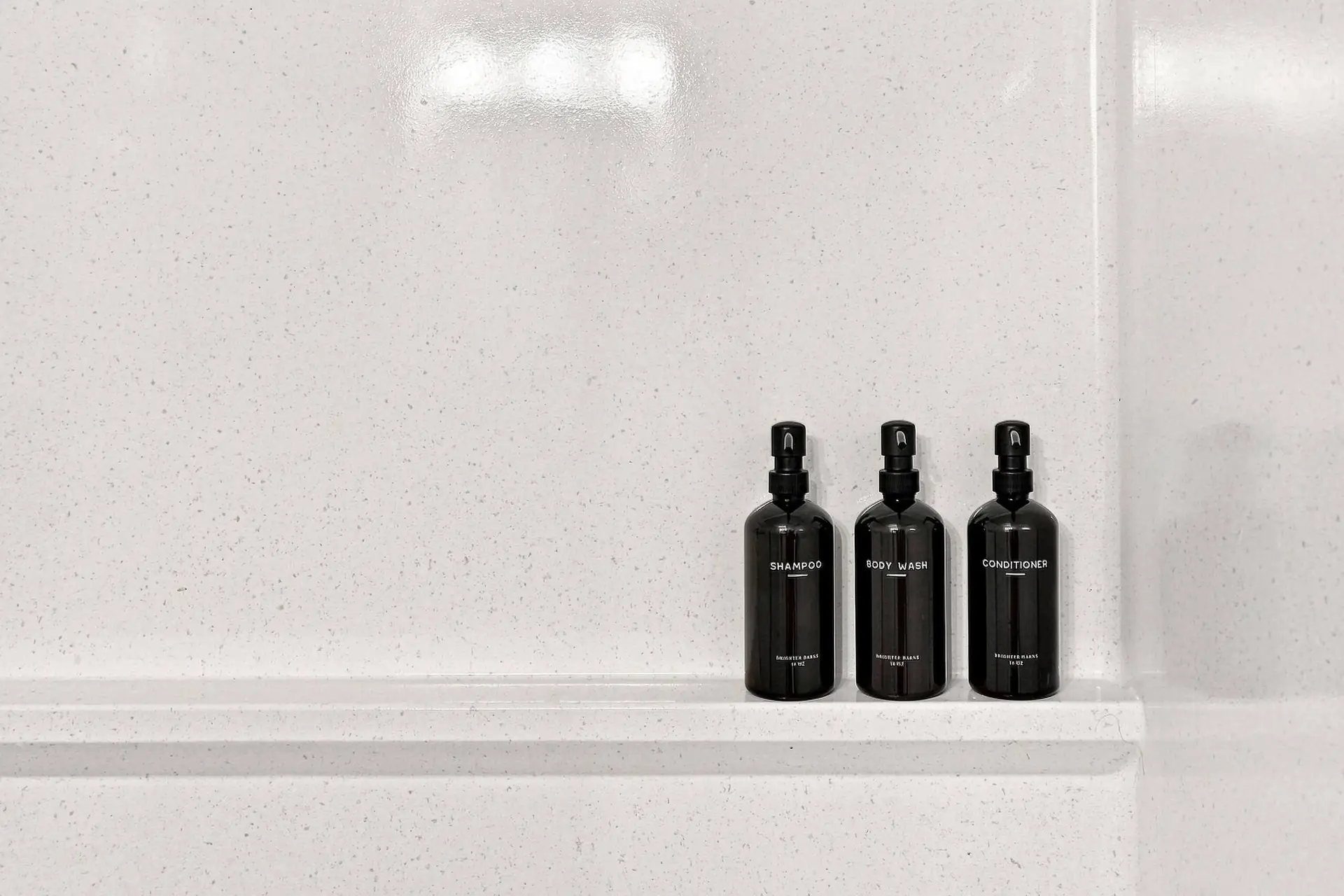 Refillable shampoo, body wash and conditioner bottles lined up on the shower ledge