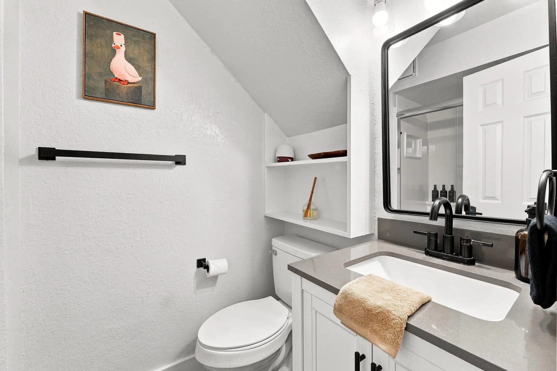 Bathroom vanity with a quartz counter, black tapware, a large framed mirror and a framed painting of a duck