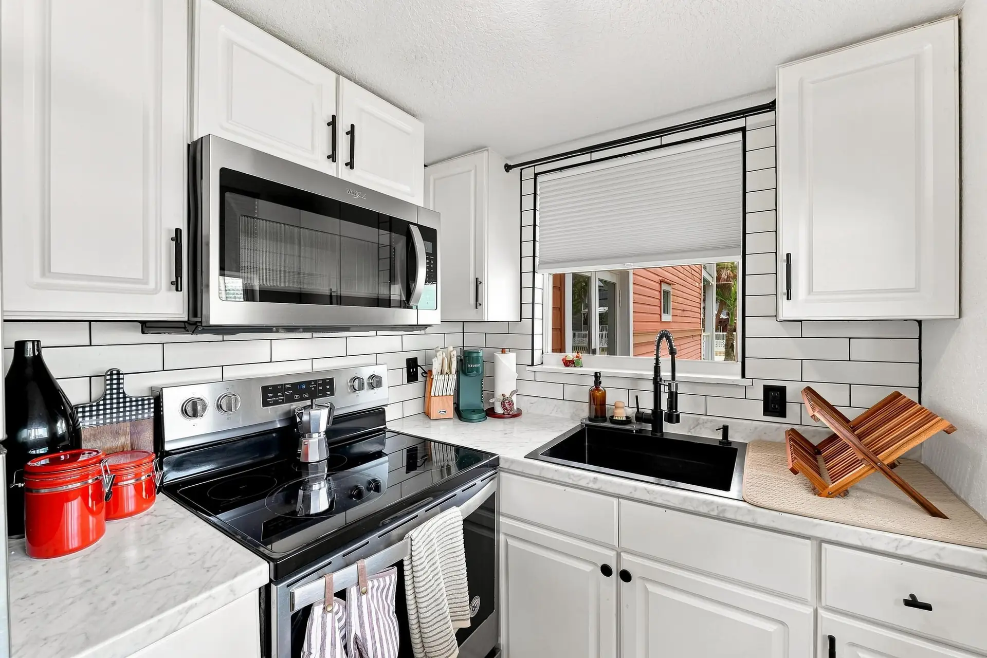 Kitchen with a stainless steel range and microwave, white subway tile backsplash, marble-look counters and a black farmhouse sink under the window