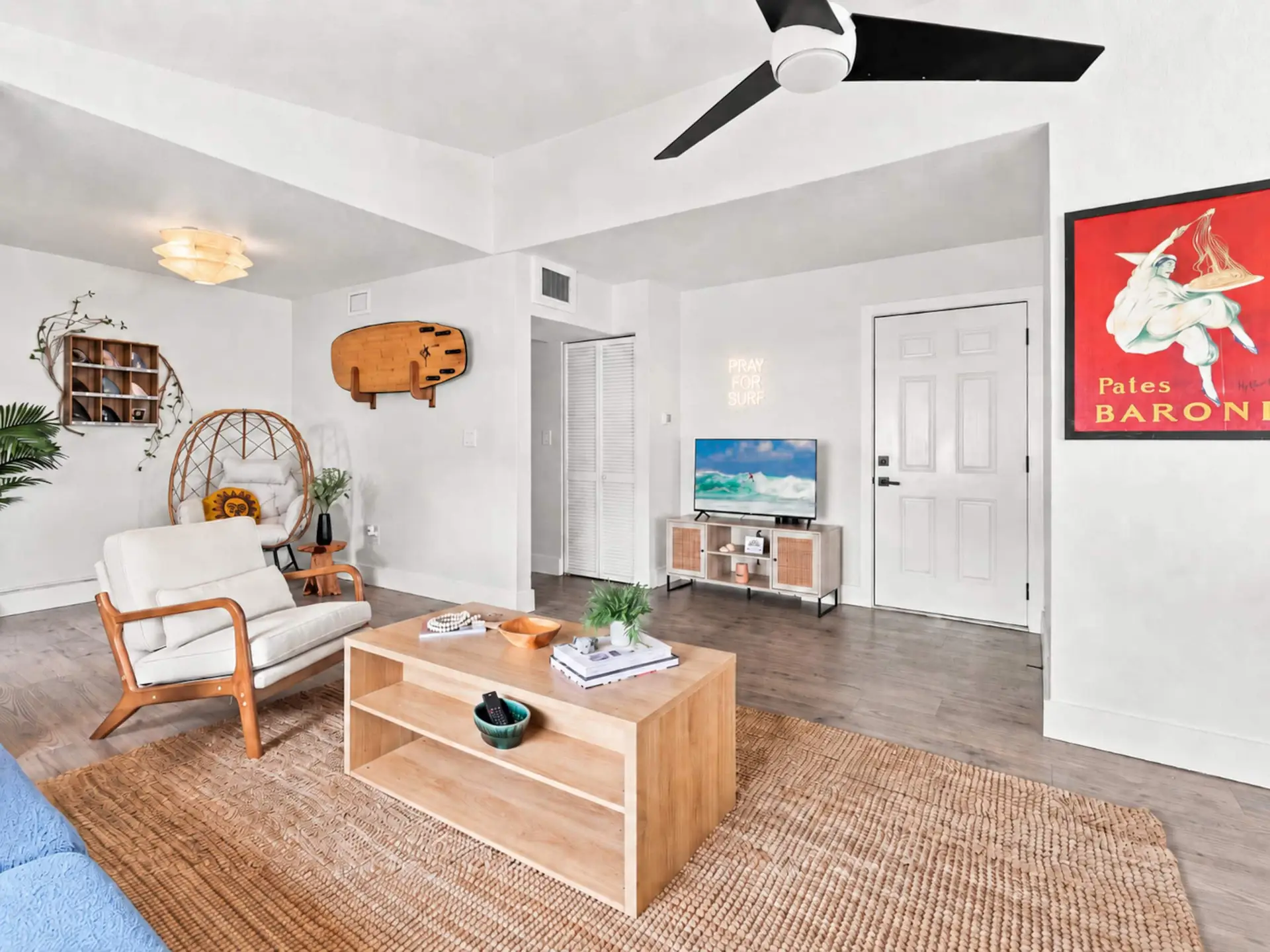 Living room corner with a hanging rattan egg chair, a wooden surfboard mounted on the wall, and a red vintage poster